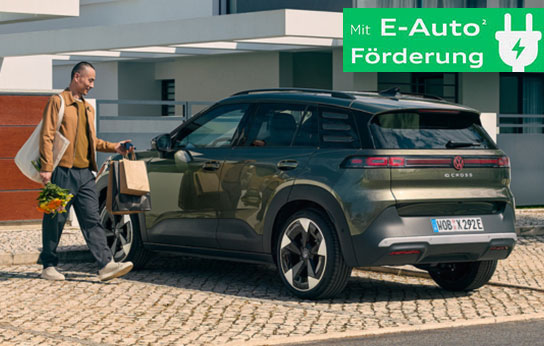 Mann mit Einkaufstüten geht an grünem Volkswagen ID.4 Cross Life SUV vorbei vor modernem Gebäude mit grünem Schild 'Mit E-Auto Förderung'